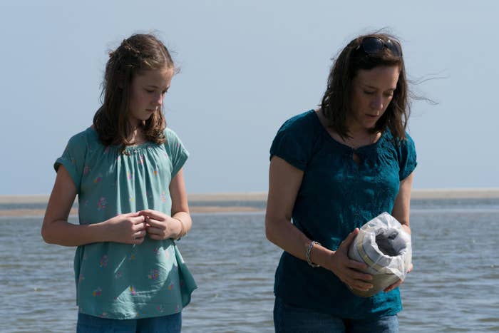 Leah Thompkins and Chloe Sevigny stand on a beach, with Chloe holding a container