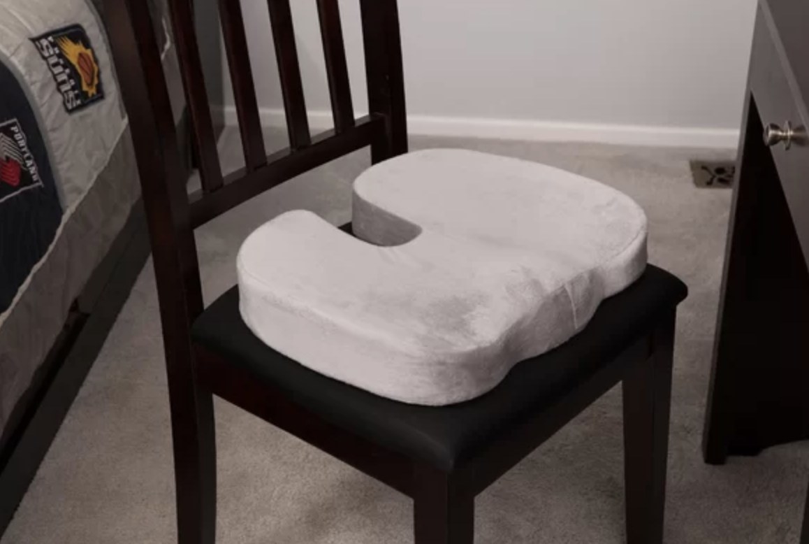 The gray plush cushion is on a dark chair and has a small indent and curved edges