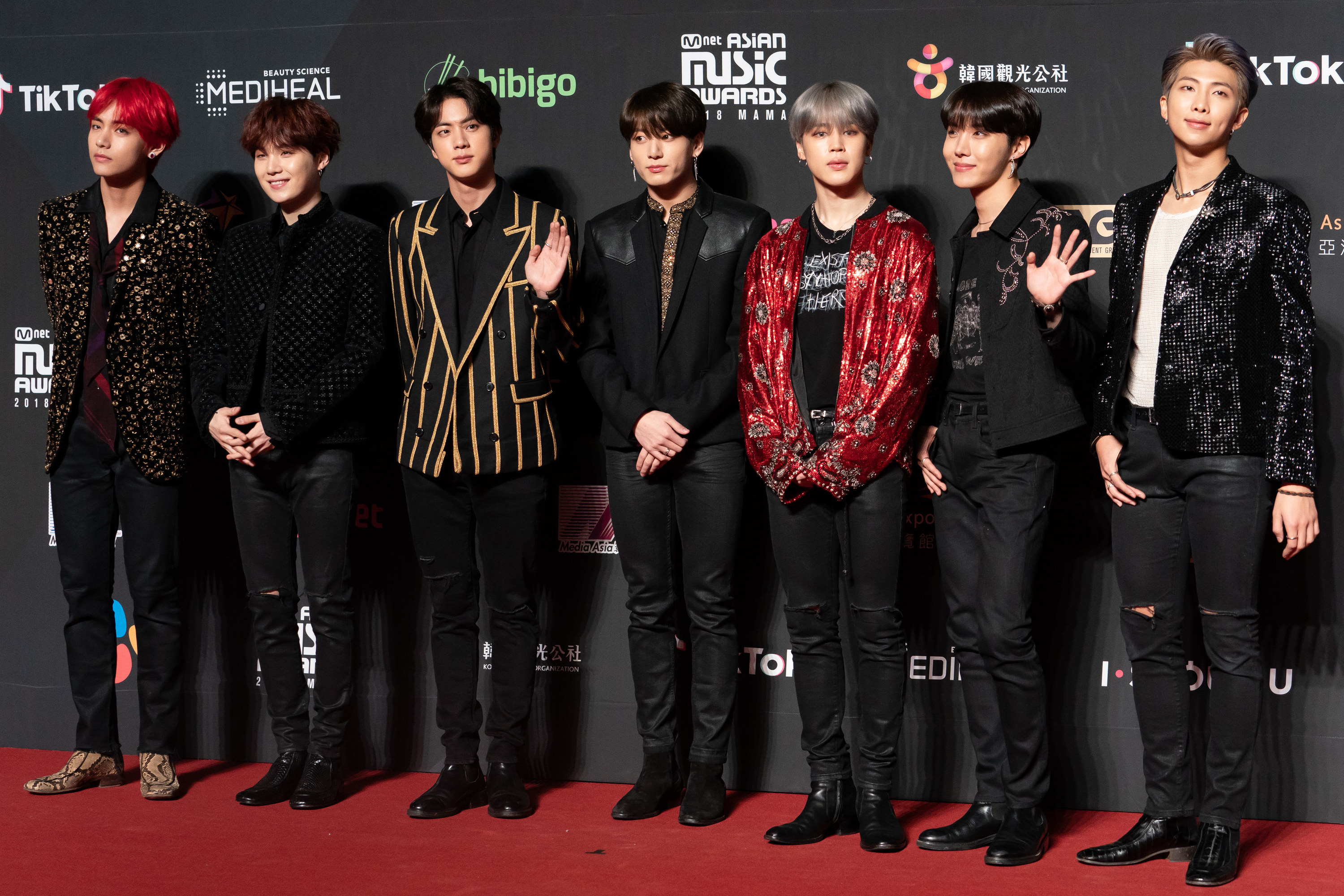 BTS all wear black leather trousers, some with small rips over the knees, but with a variety of blazers ranging from black with gold stars to gold pinstripes, leather shoulders, bright red with circular detailing, and black and covered in sequins