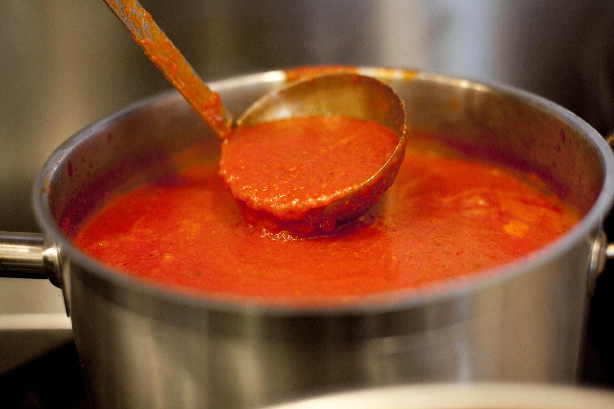 A ladle in a pot of marinara sauce.