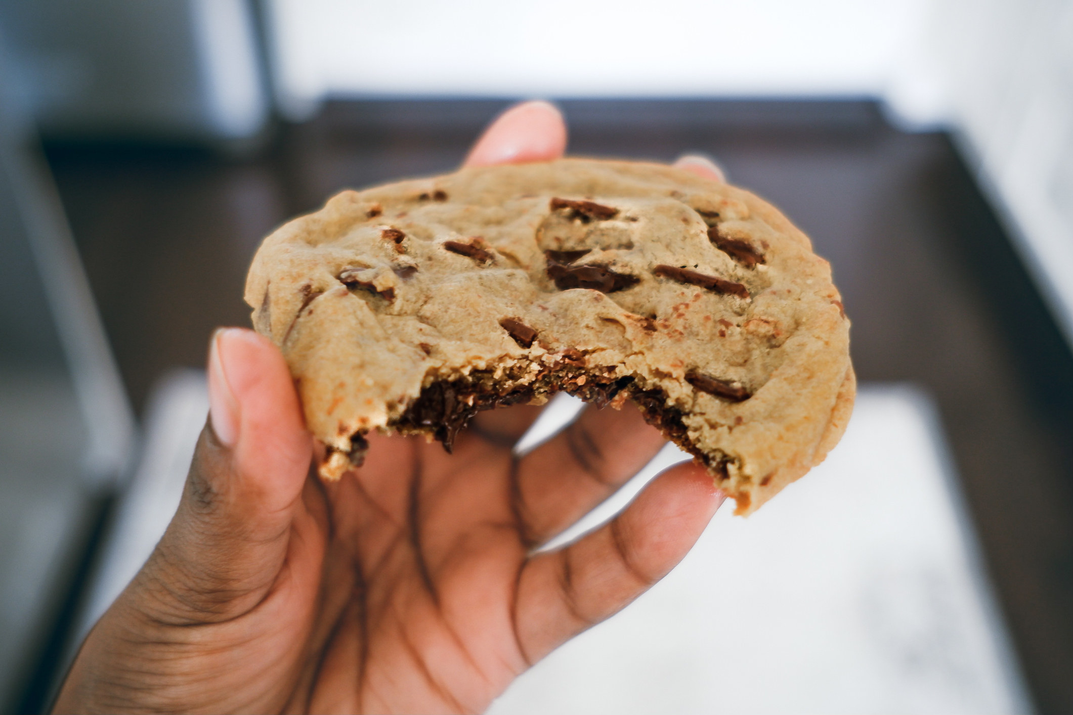 A woman holding a partially eaten chocolate chip cookie.