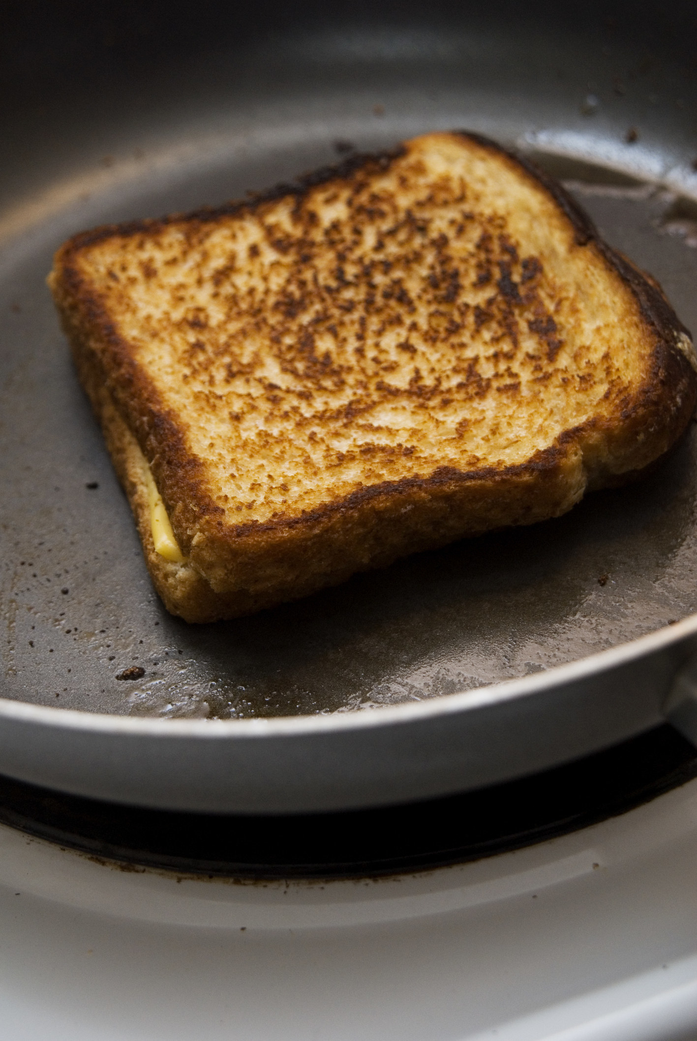 A crispy grilled cheese sandwich in frying pan on stove.