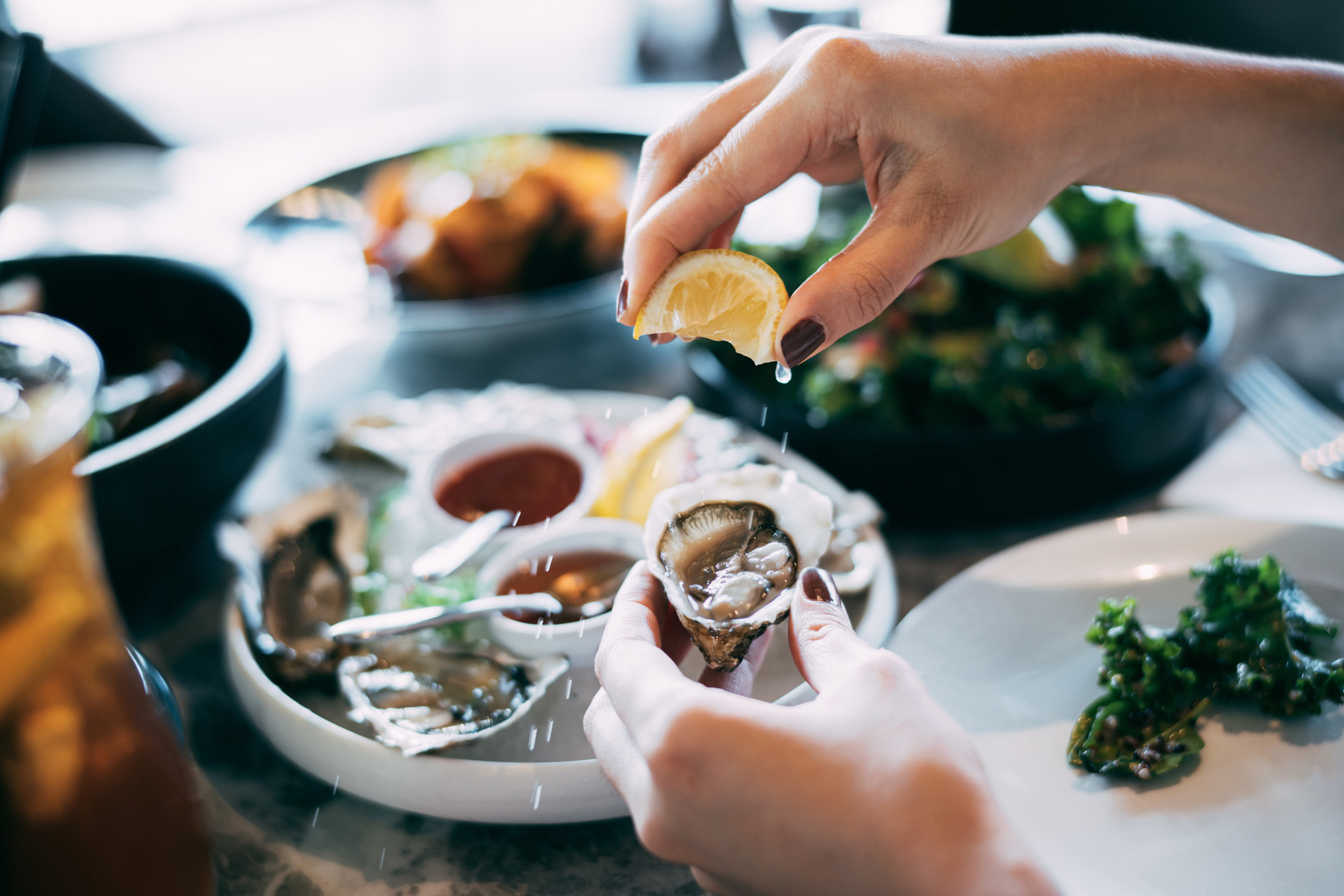 A woman&#x27;s hand squeezing lemon juice on to a fresh oyster.