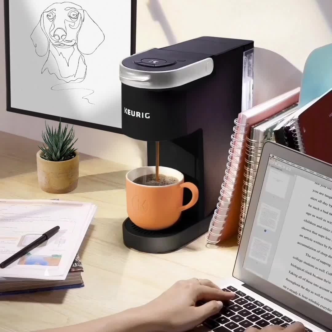 A person at a desk with a Keurig coffeemaker beside their laptop