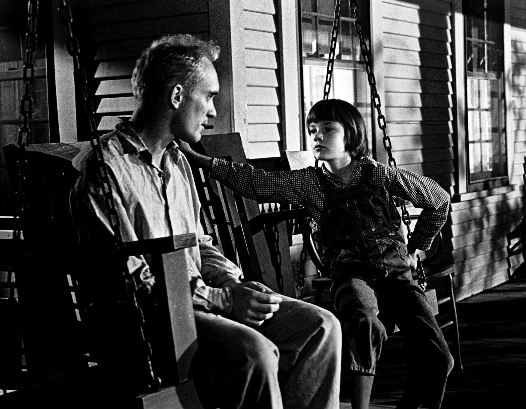 black and white still of characters sitting on a porch swing in How to Kill a Mockingbird