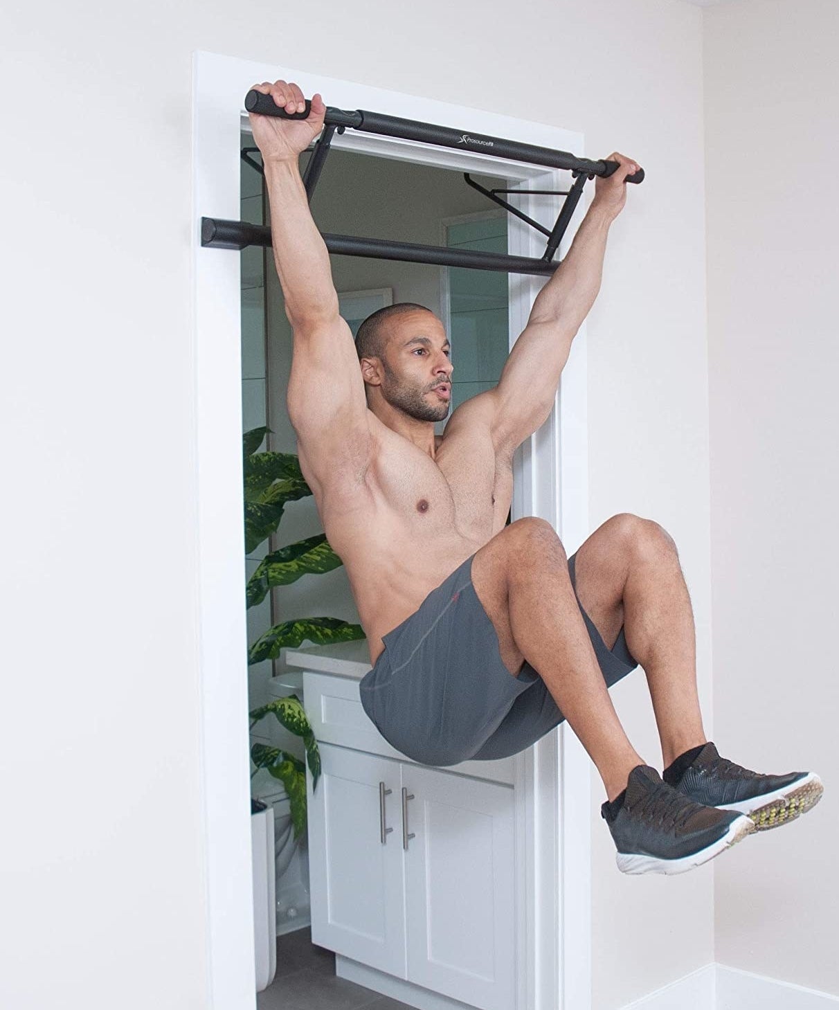Model doing a pull-up with the black bar attached to a door frame