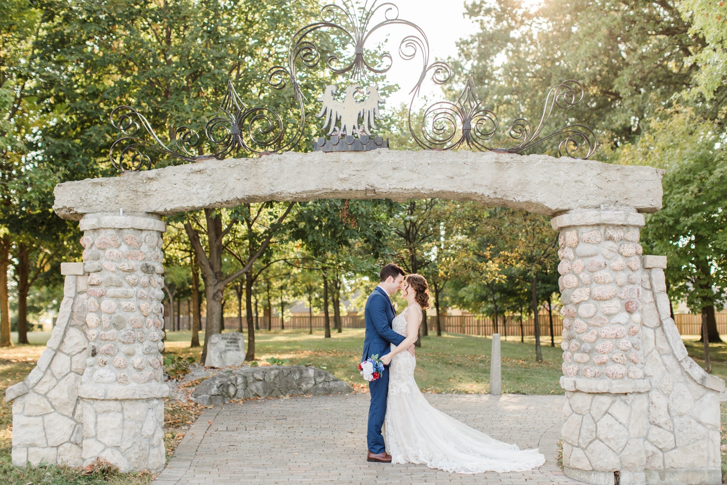 Bride and Groom embracing beneath a stone archway topped with a metal bird