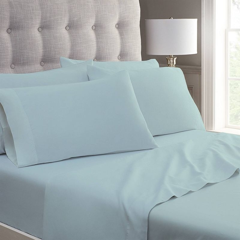 A crisp made bed with a plush headboard and blue folded sheets