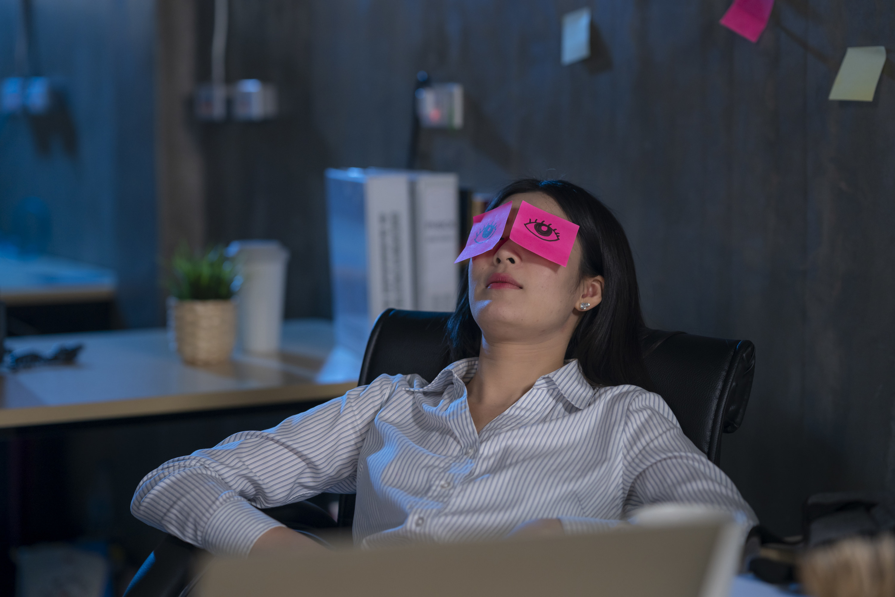 Woman sleeping at her desk with post it notes over her eyes