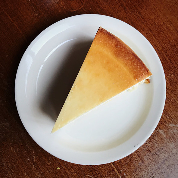 A slice of plain cheesecake on a plate, seem from above