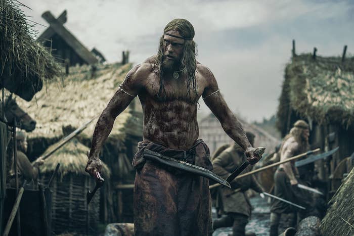 Alexander Skarsgård standing outside holding weapons in a scene from The Northman