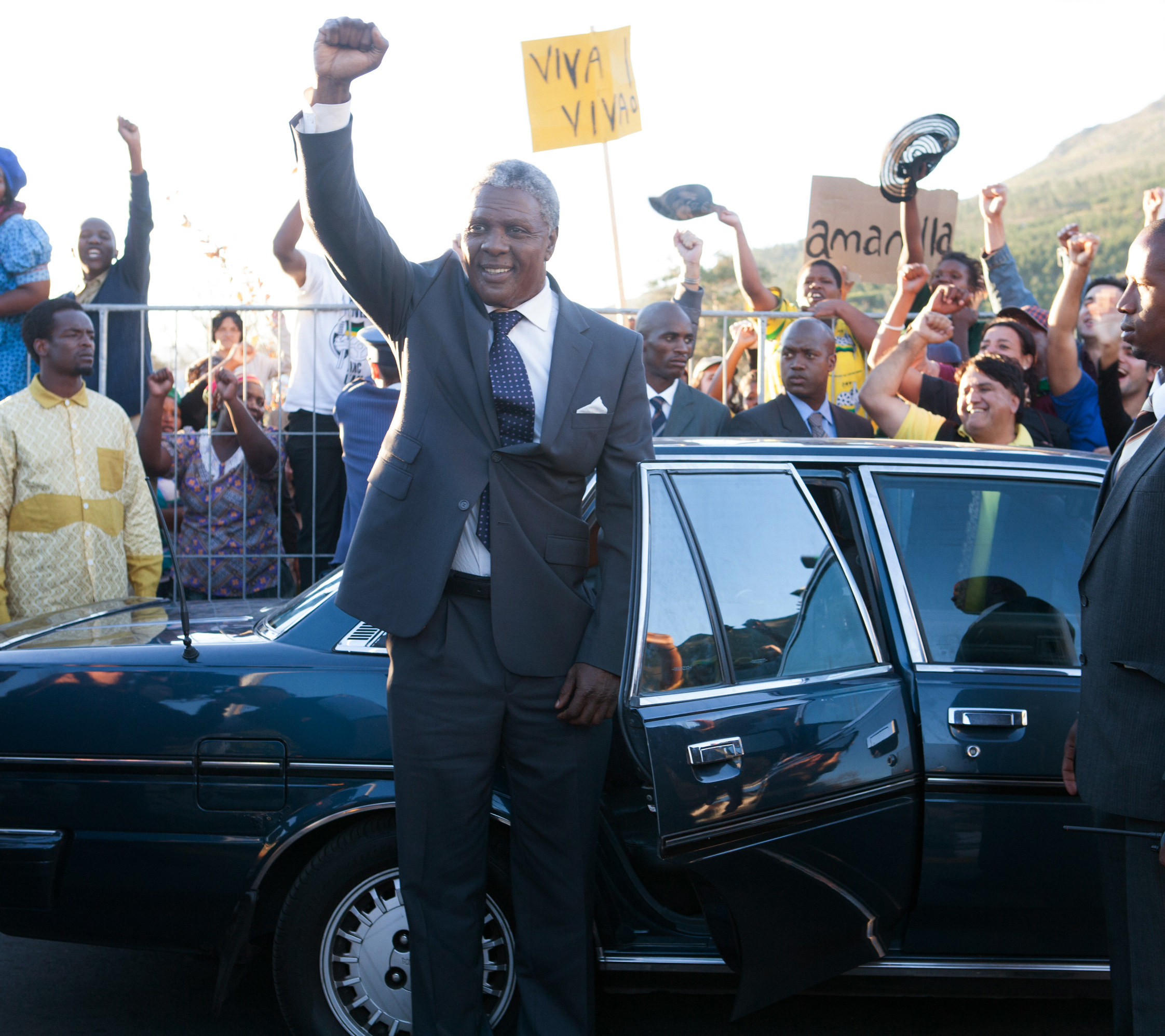 Elba raising his fist as he gets out of a car with a crowd of people behind him