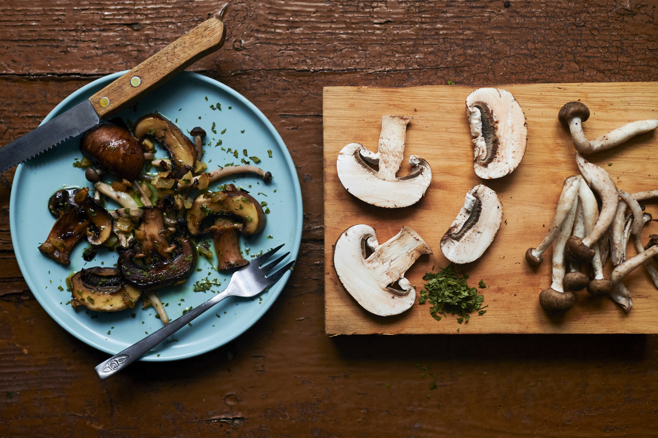 Different types of mushrooms on a plate and a cutting board, raw and cooked