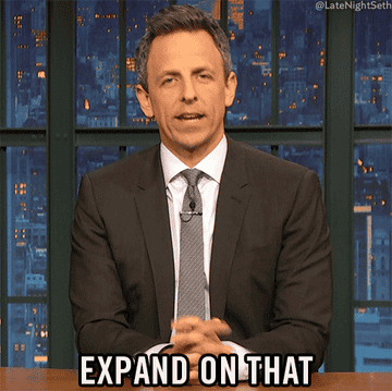 The titular host of Late Night with Seth Meyers sitting at his desk and asking to &quot;Expand on that&quot;.