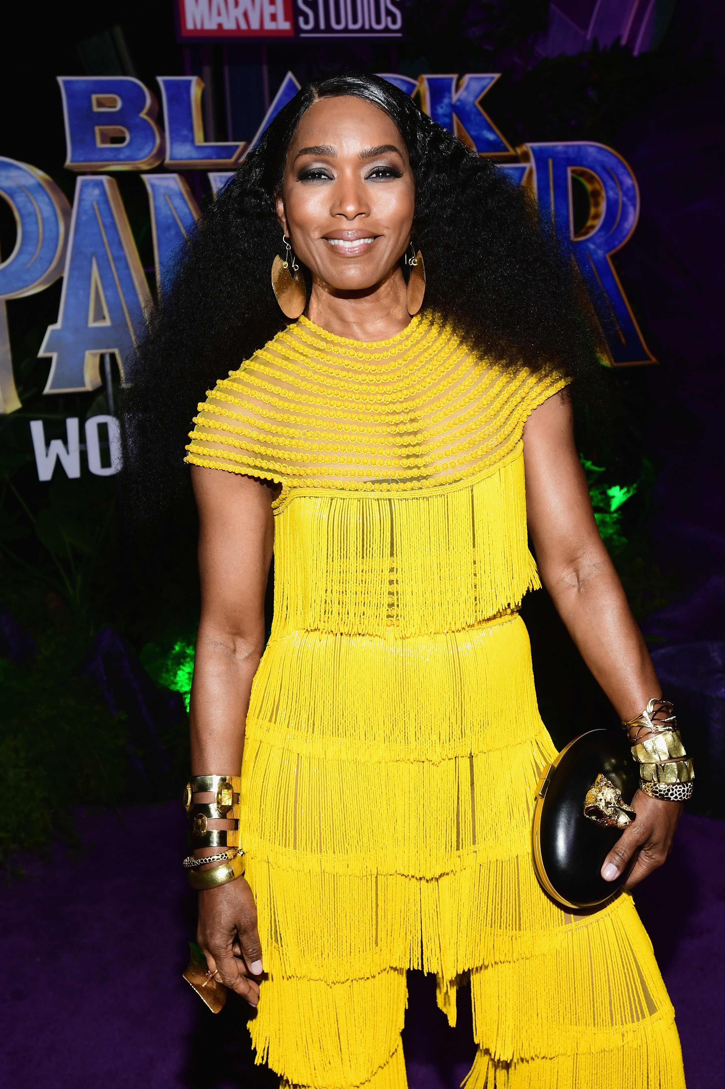 Angela smiling at the Black Panther premiere, wearing a yellow fringed jumpsuit