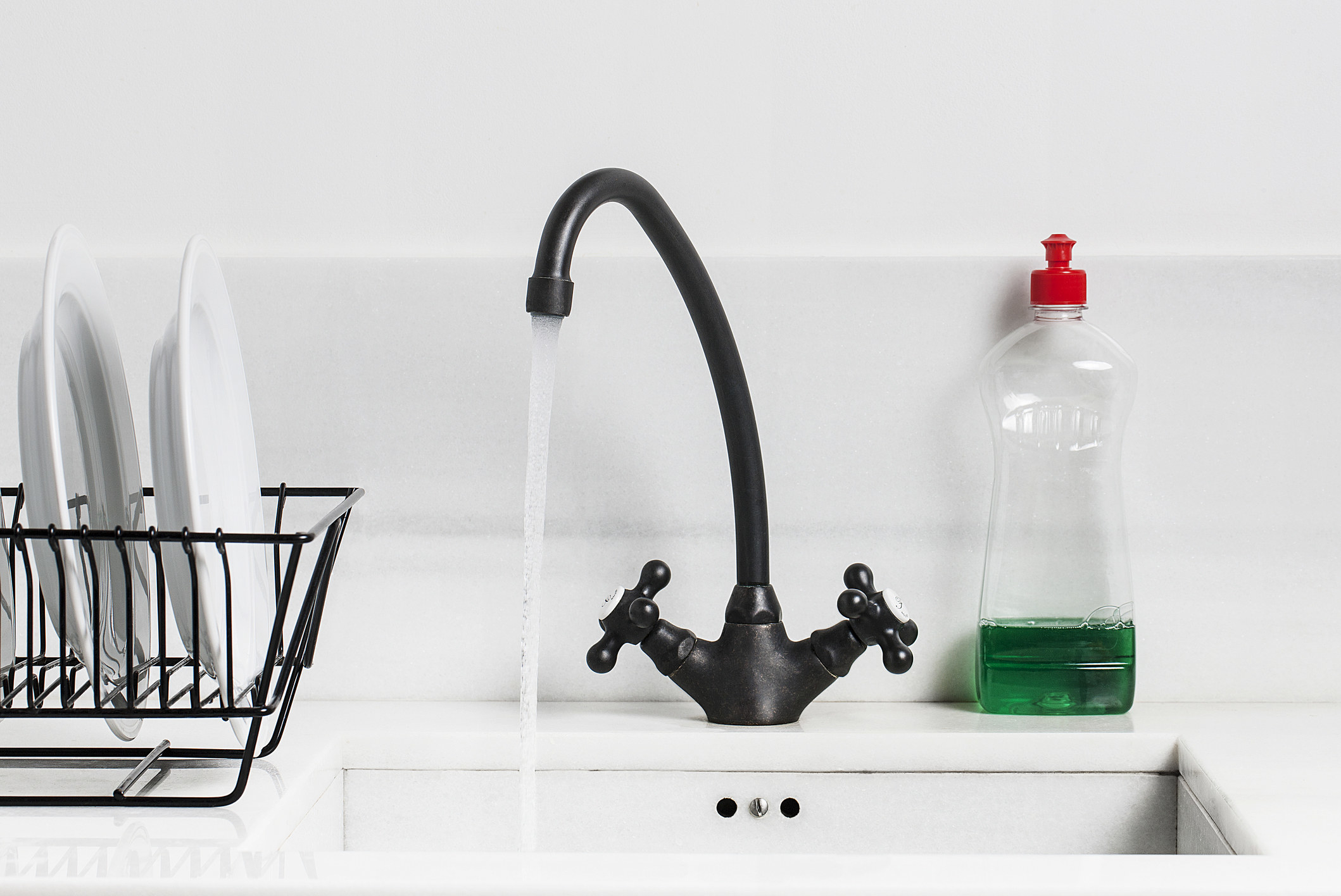 A sink with running water, dishwashing detergent, and clean dishes on a rack.
