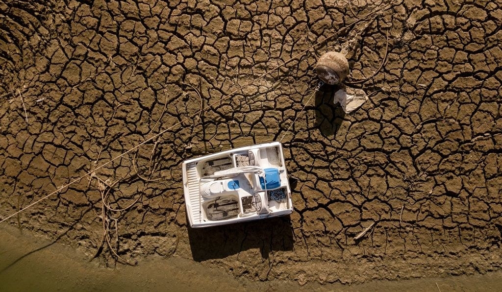 A boat lays abandoned on ground that&#x27;s so dry it looks like desert