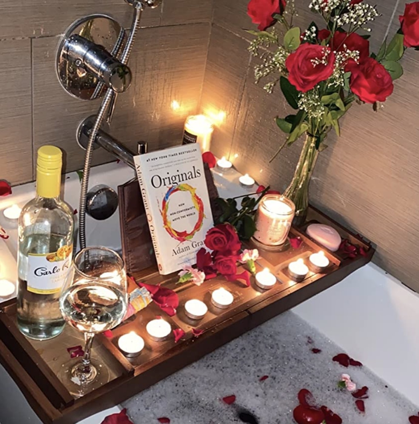 reviewer photo showing the bath caddy topped with a book,  wine, flowers and candles