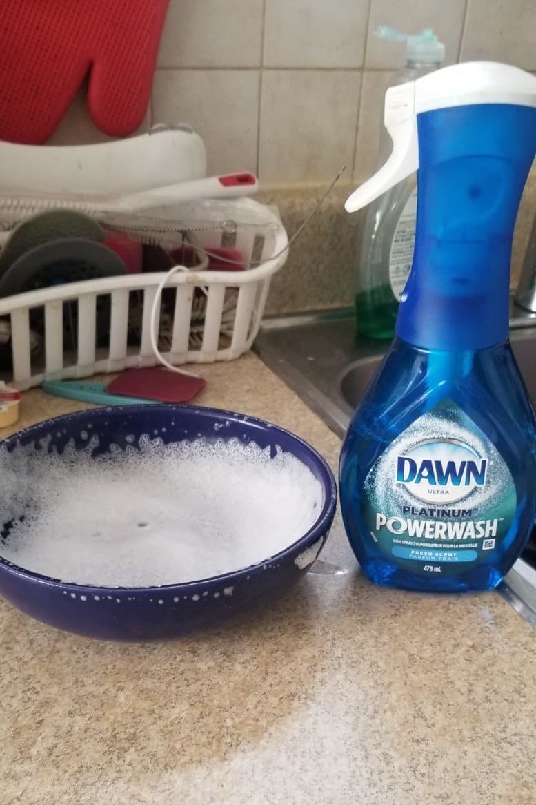 A bowl covered in washing foam next to the bottle of dish soap