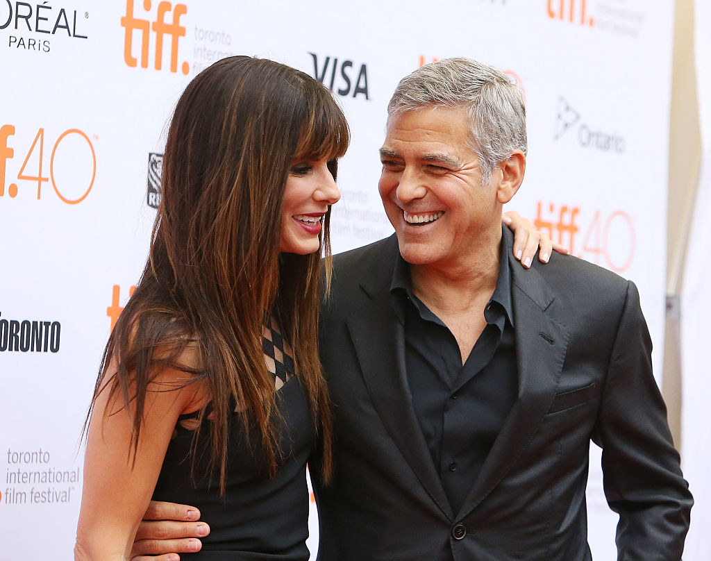 Sandra and George smiling and hugging on the red carpet