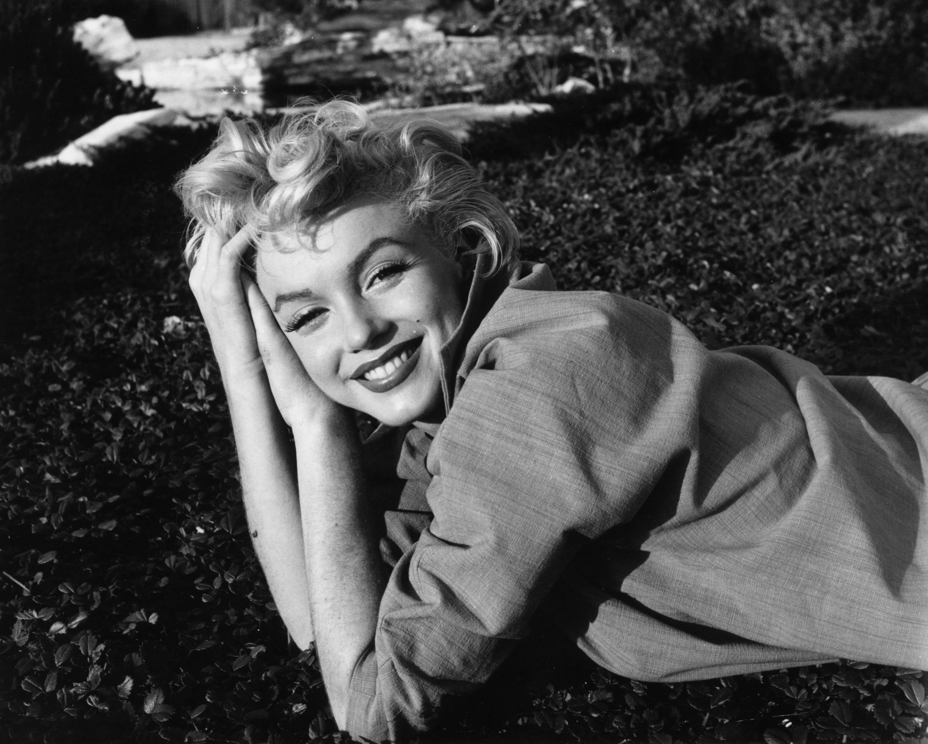 Marilyn Monroe smiling and laying in the grass.