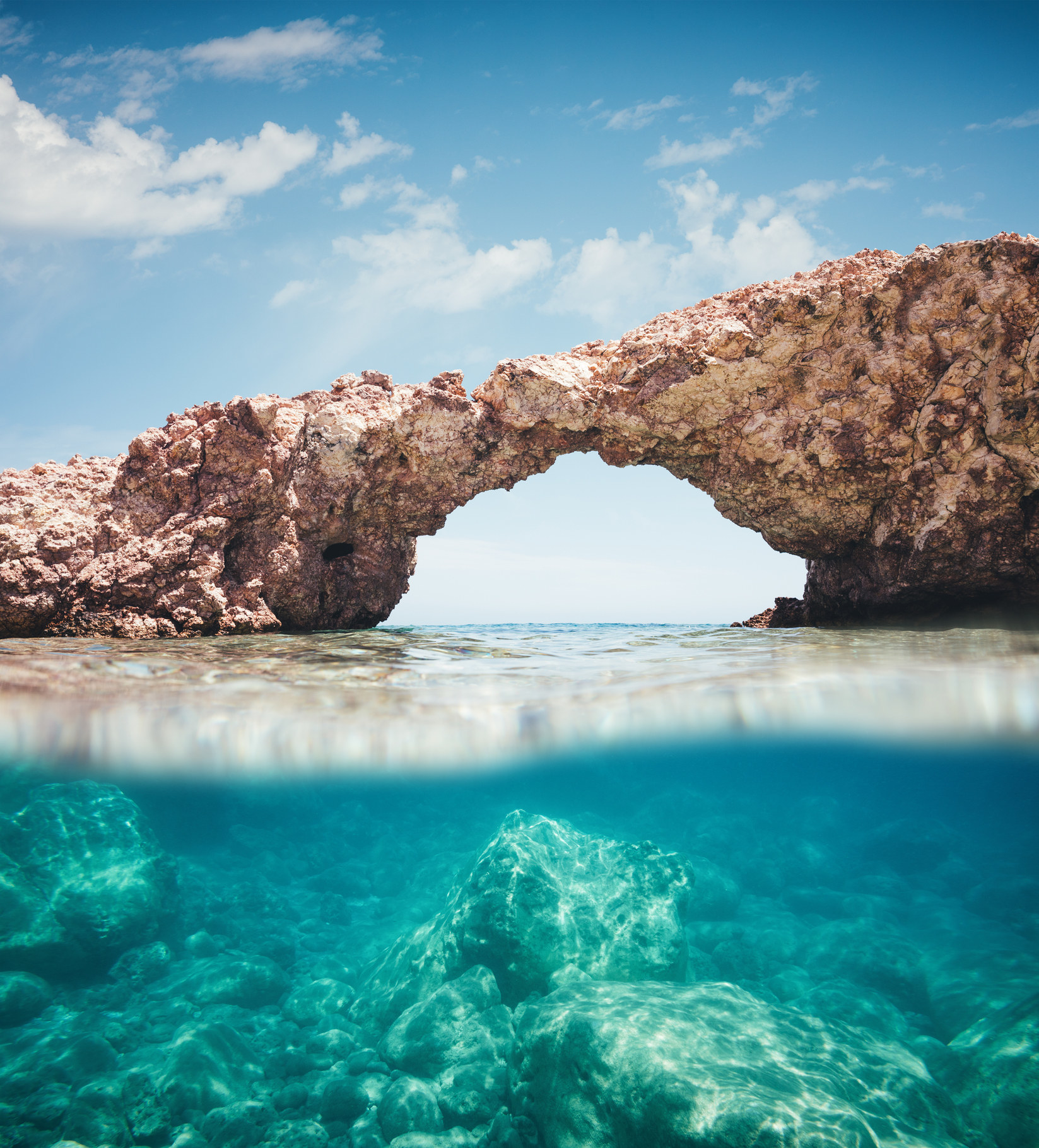 View from the water on natural rock arch on Milos Island.