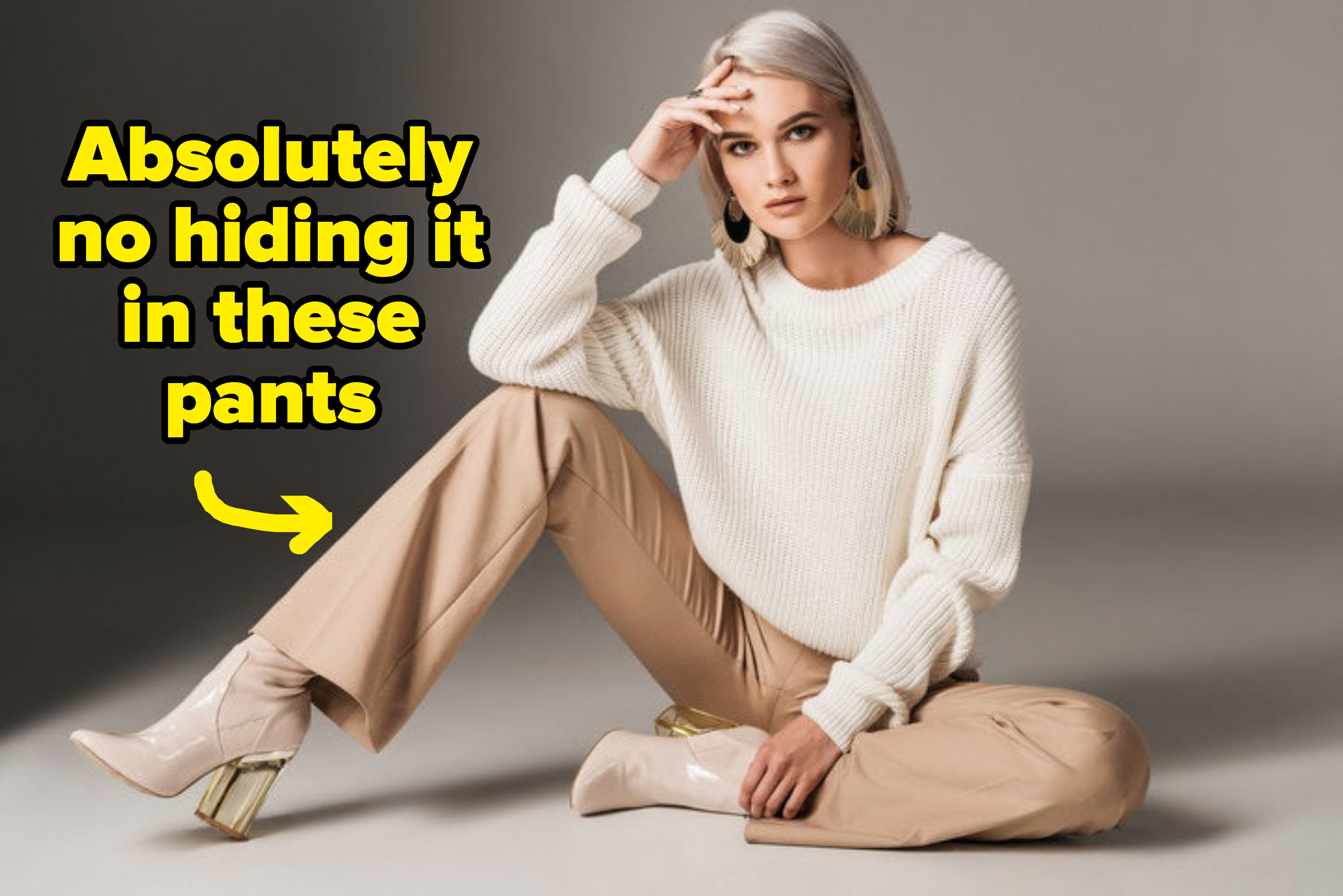 fashionable woman posing in white trendy sweater, beige pants, and autumn heels, on gray, with the text &quot;absolutely no hiding it in these pants&quot;