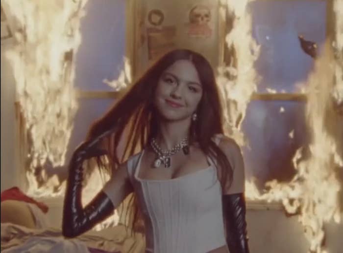 Olivia Rodrigo smiling in front of a room that&#x27;s on fire