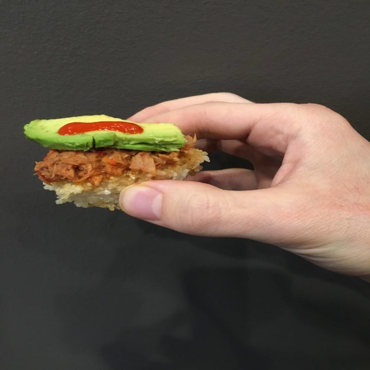 The writer holding a piece of spicy tuna over crispy rice with avo and a drizzle of Truff hot sauce