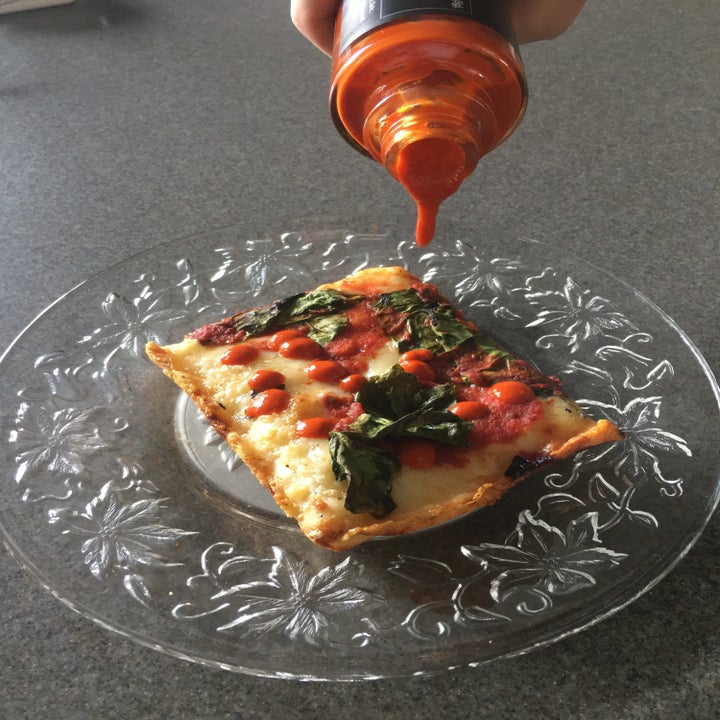 Some Truff hot sauce being drizzled over Buddy's square Detroit-style pizza
