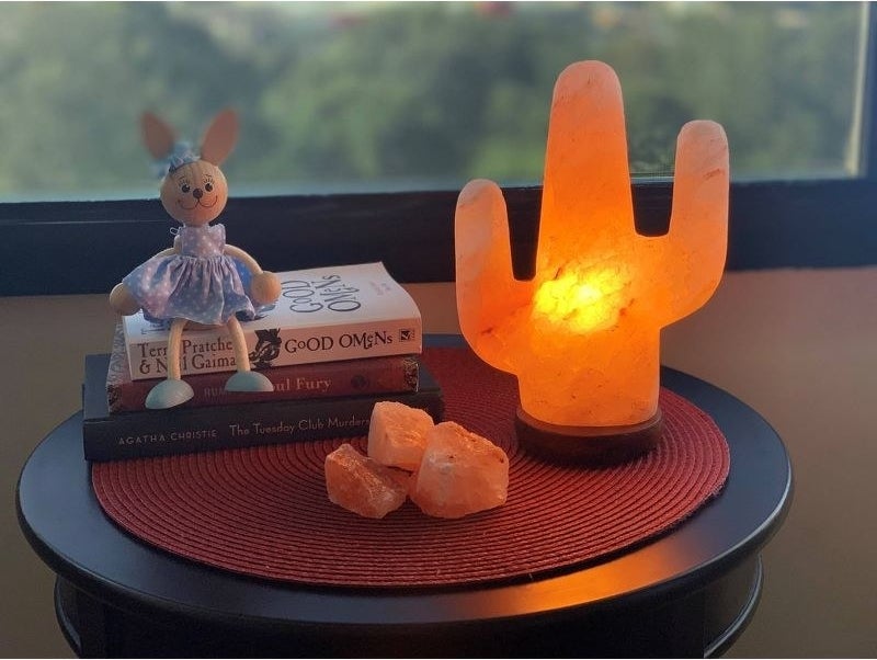 Glowing salt lamp set on round surface in room near decorative stack of books