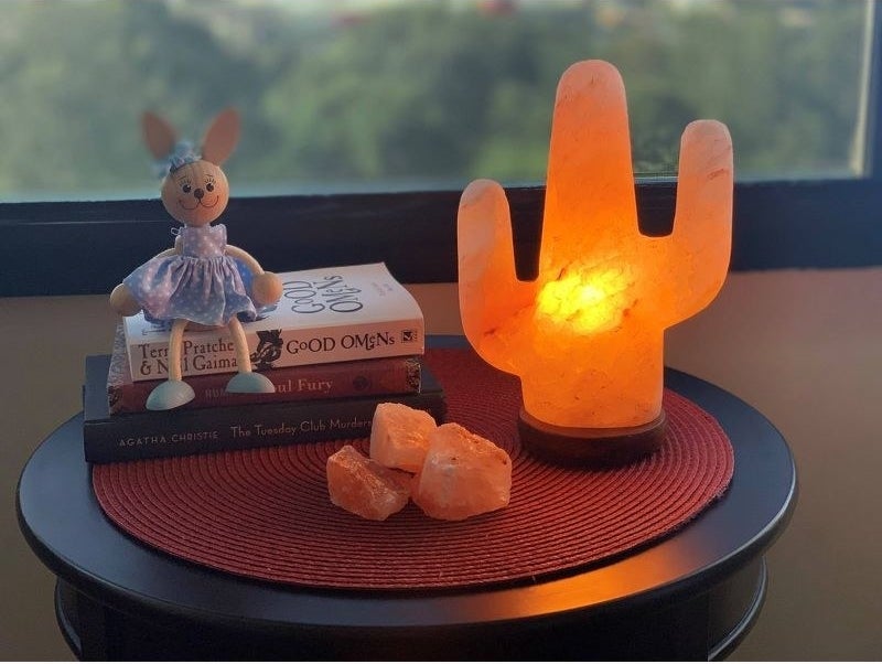 Glowing salt lamp set on round surface in room near decorative stack of books