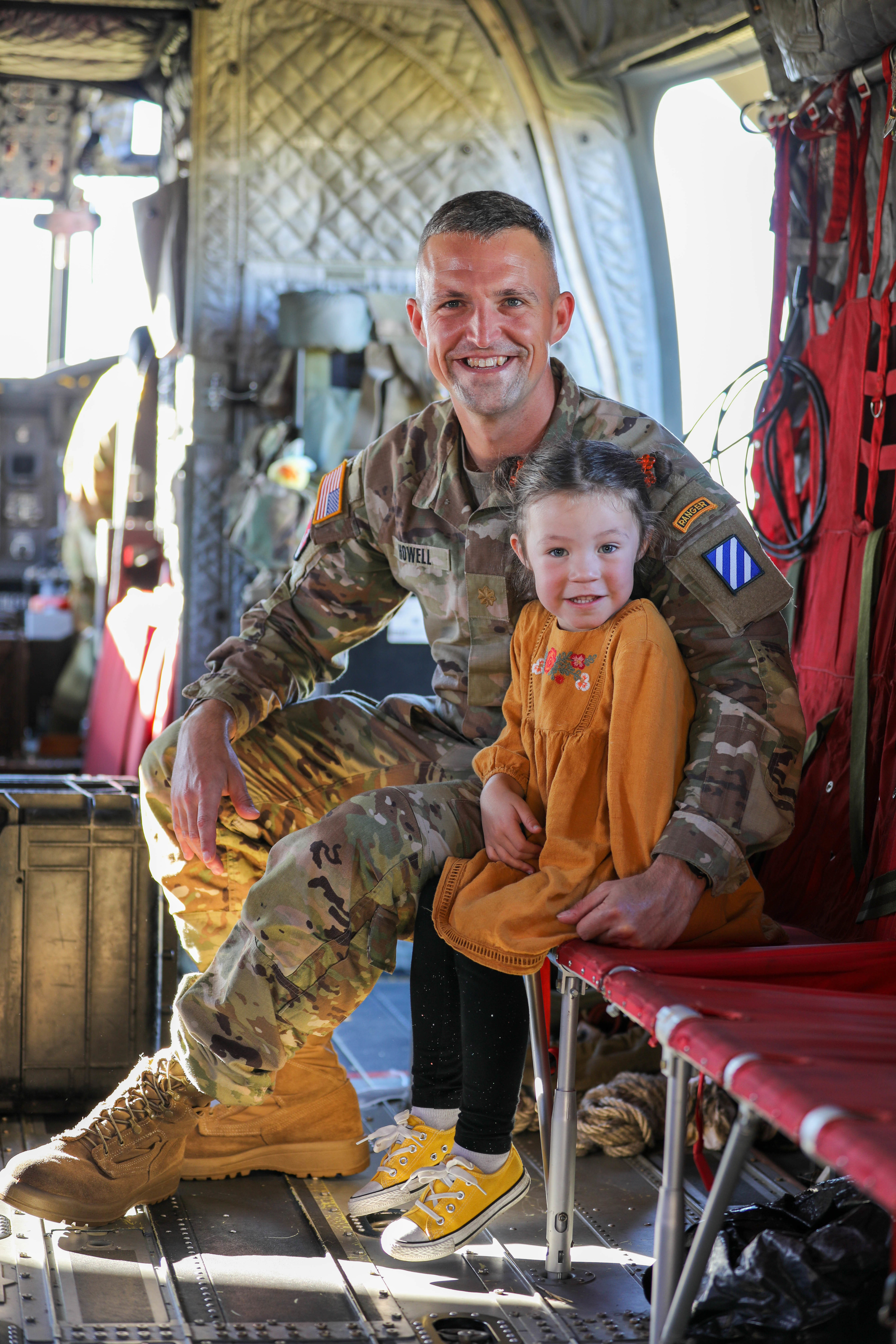 A US Army member sits inside an aircraft with his young daughter