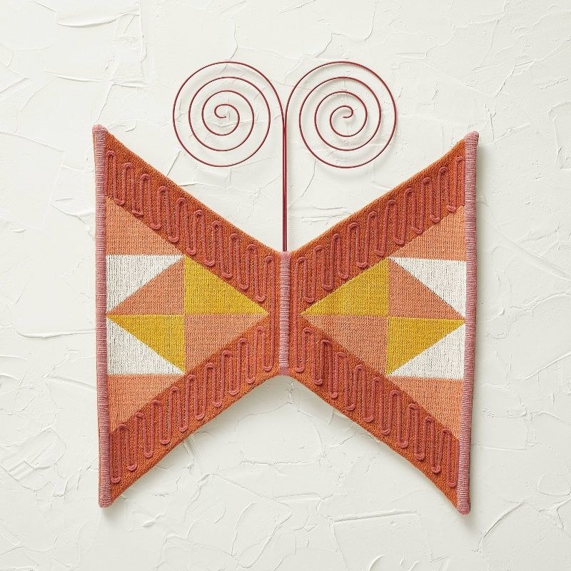 Multicolored, woven wall art hanging on white, textured background
