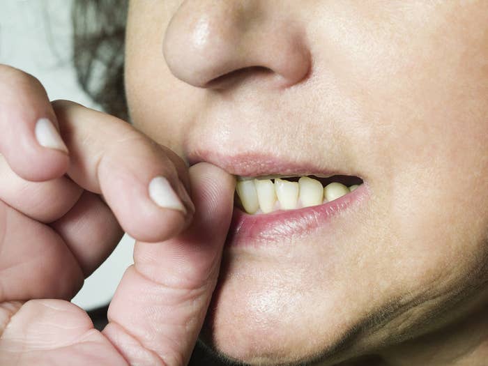 A close-up of a woman biting her thumb nail