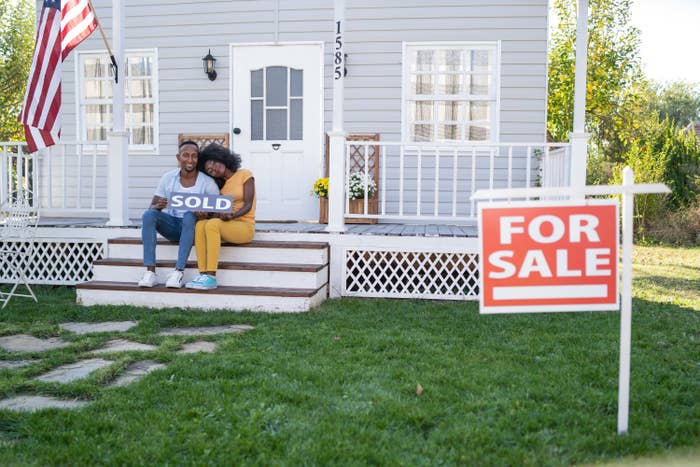 woman leans head on partner&#x27;s shoulder as they sit on the porch of the house they just bought or sold