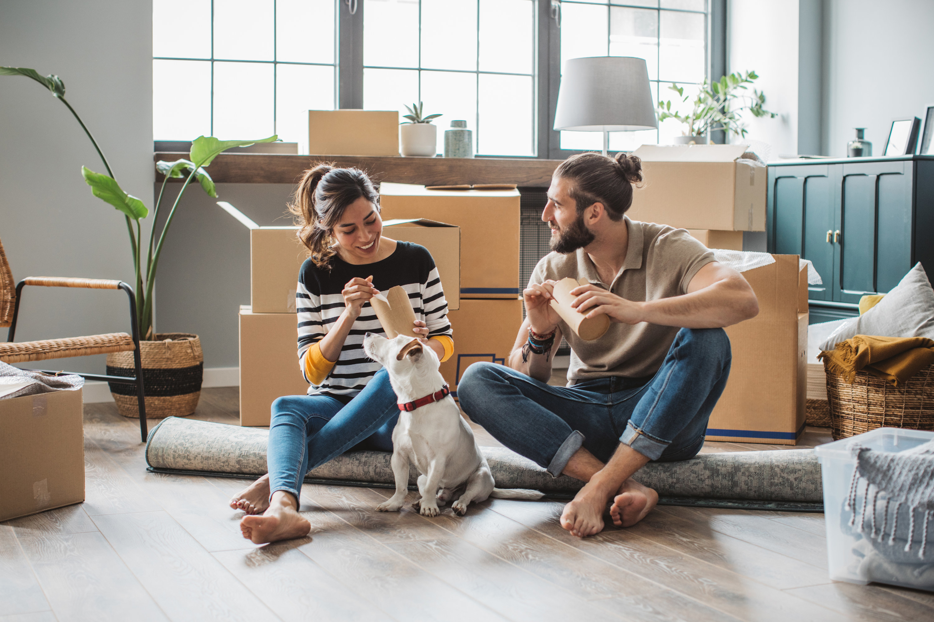 couple eating takeout on the floor with their dog during moving
