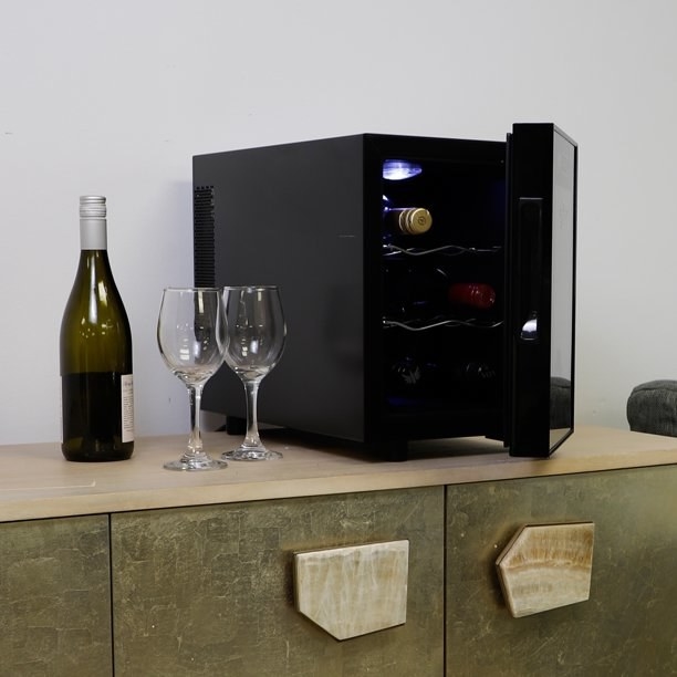 The wine fridge sits on a countertop next to wine glasses and a bottle of wine