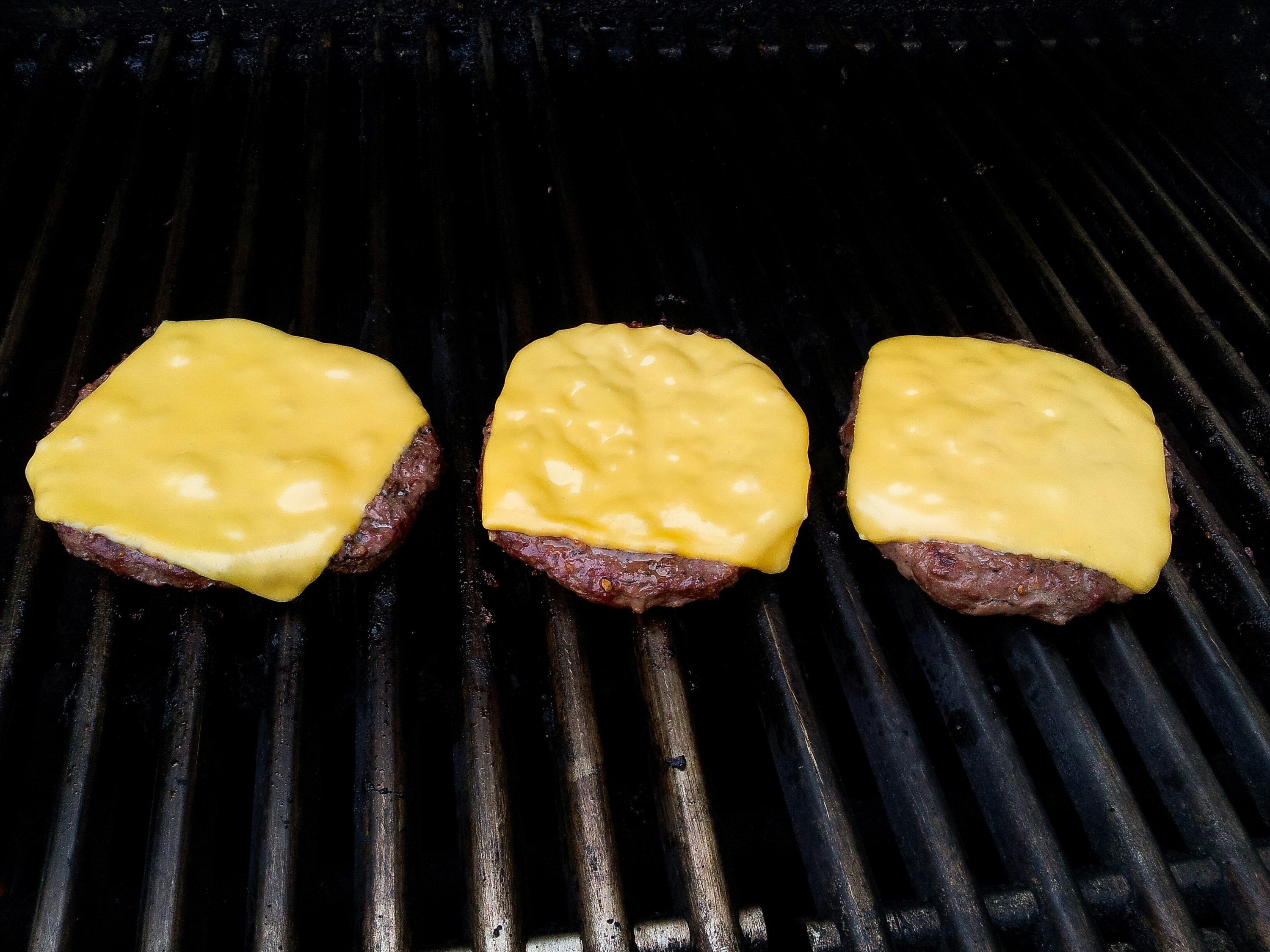 Three cheeseburger patties on a grill