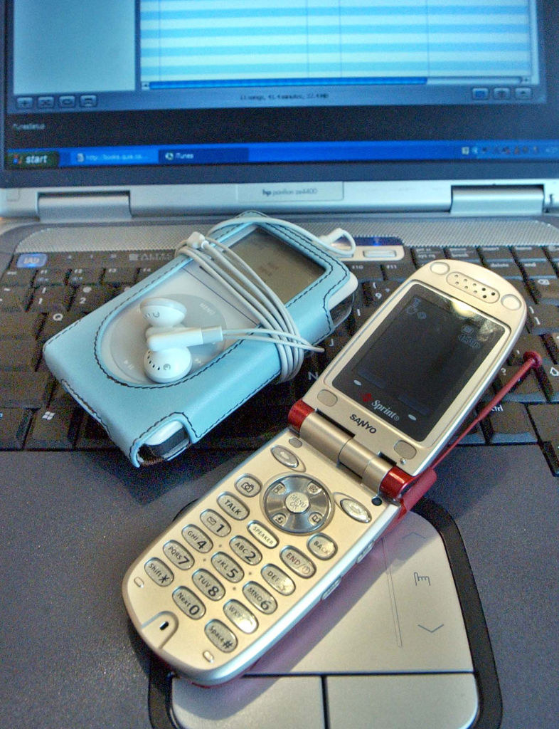 An iPod in a case with earbuds next to an open flip phone