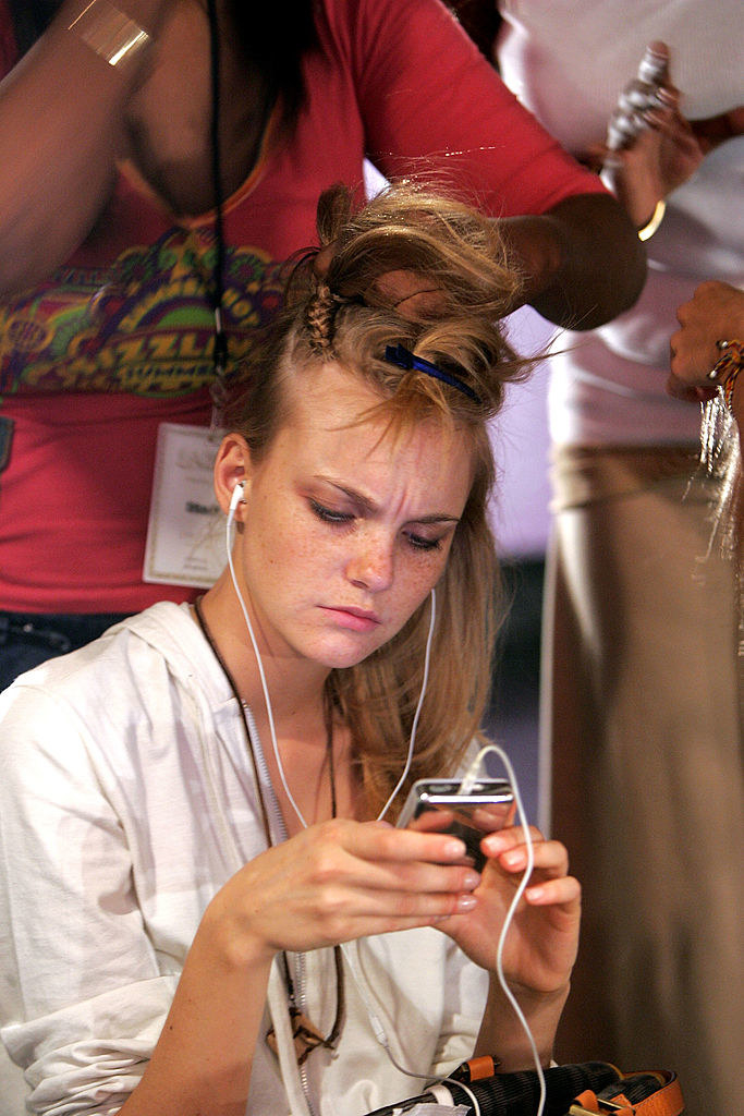 A young woman with earbuds listening to her iPod as someone does her hair