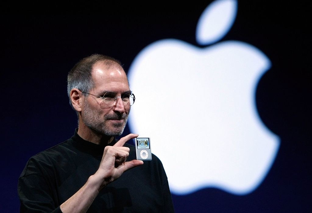 Steve Jobs holding up a tiny iPod with the Apple logo in the background