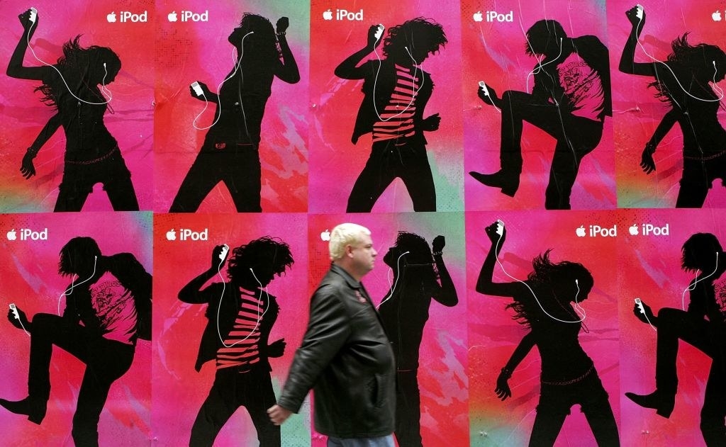 Person walking by an iPod ad showing silhouettes of people dancing while listening to them