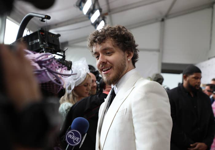 A man in a suit speaks to cameras on a red carpet 