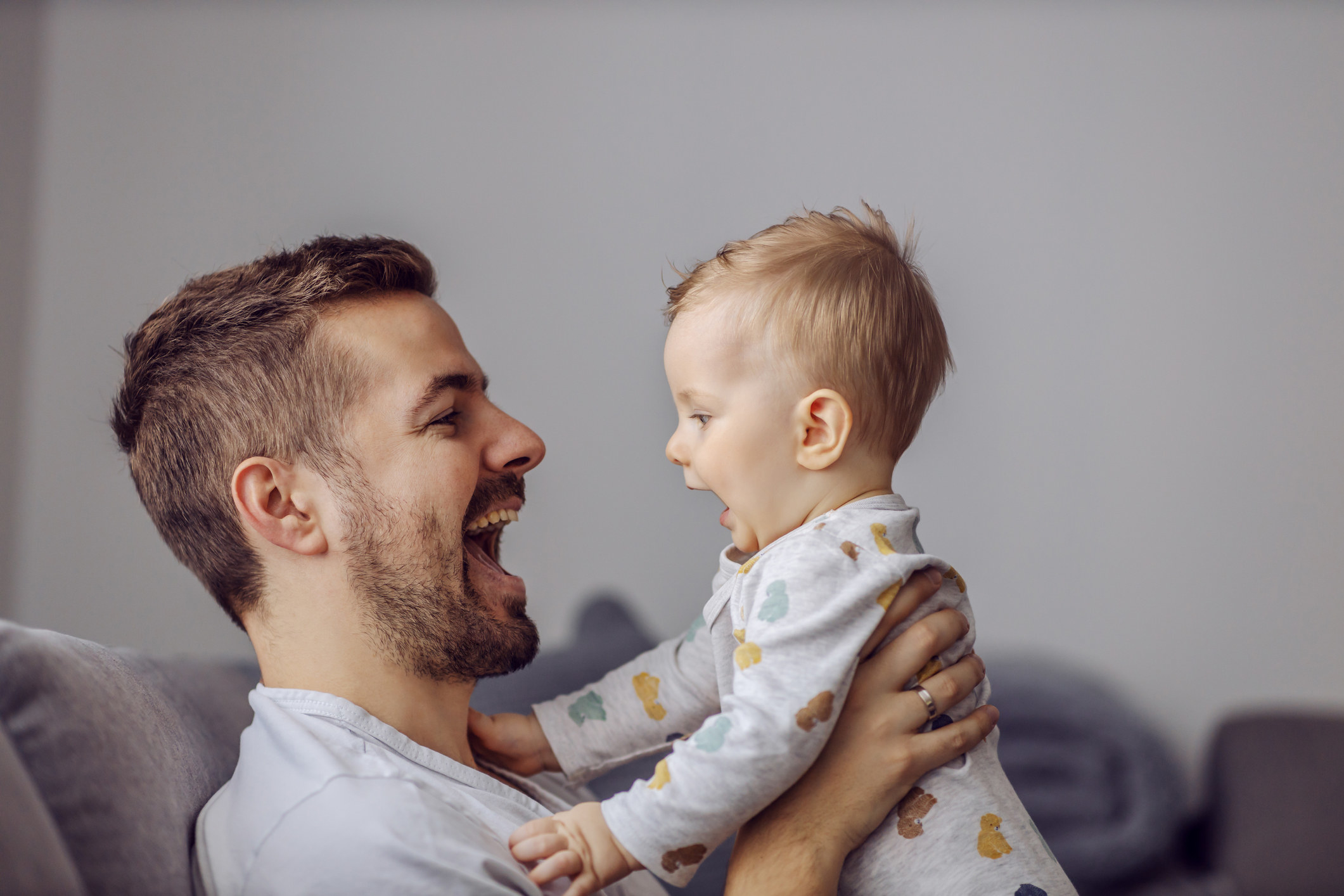 A father opens his mouth and smiles as he holds his baby