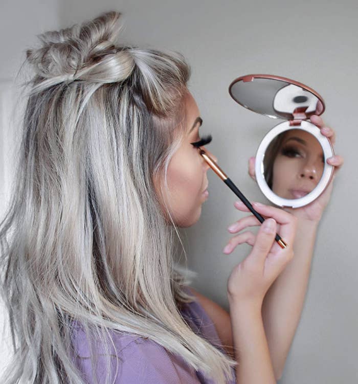 Someone using a a makeup brush and using the mirror with their other hand