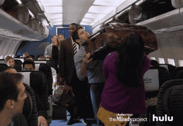 Danny Castellano helps Mindy Lahiri shove a giant suitcase into a plane overhead luggage compartment on &quot;The Mindy Show&quot;