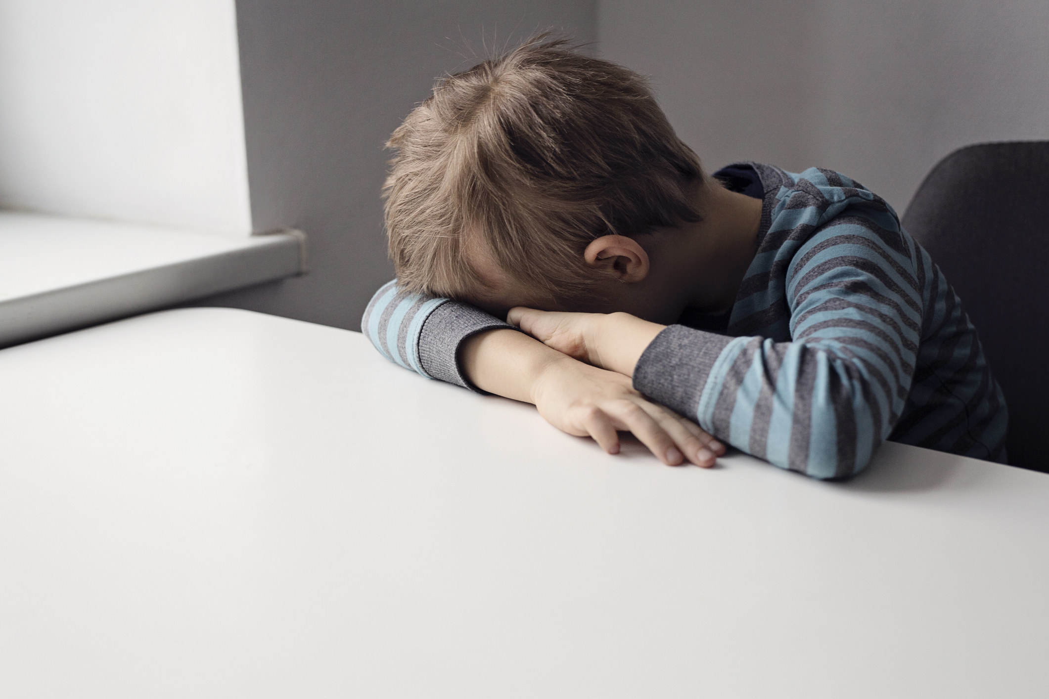 A kid laying his head in his arms on a table