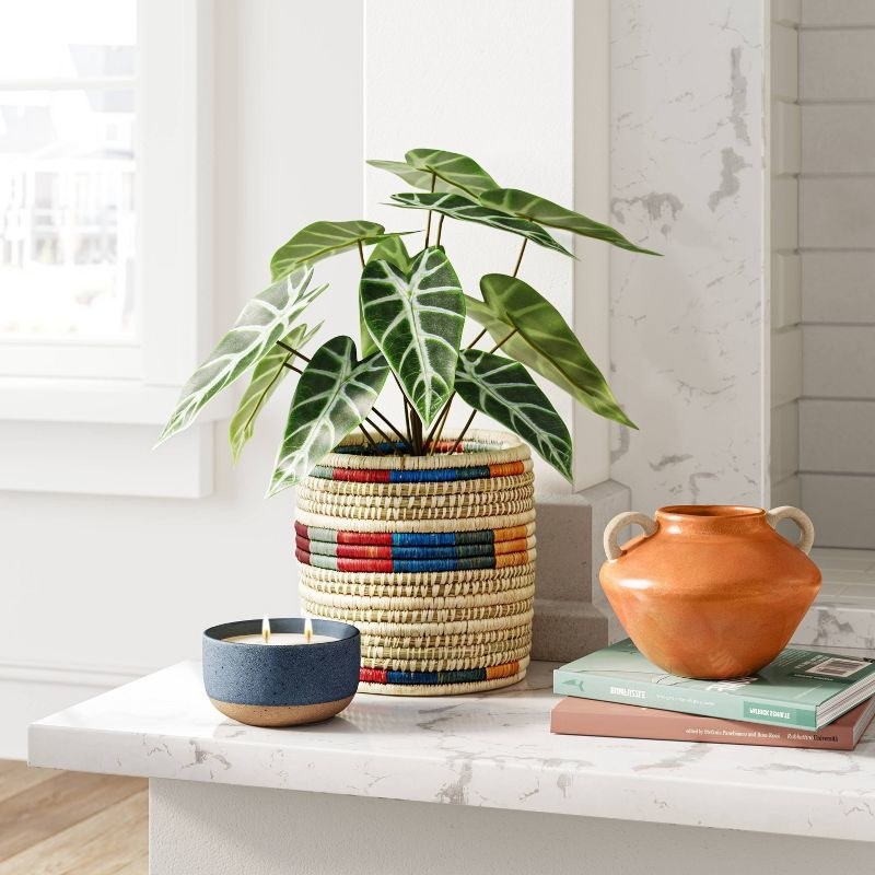 the woven planter next to a candle, books and vase