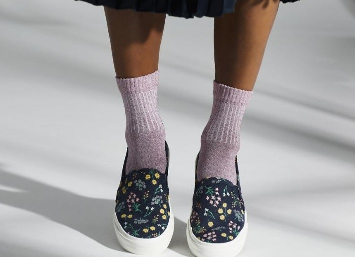 model wearing the slip-on sneakers in black with floral print all over them